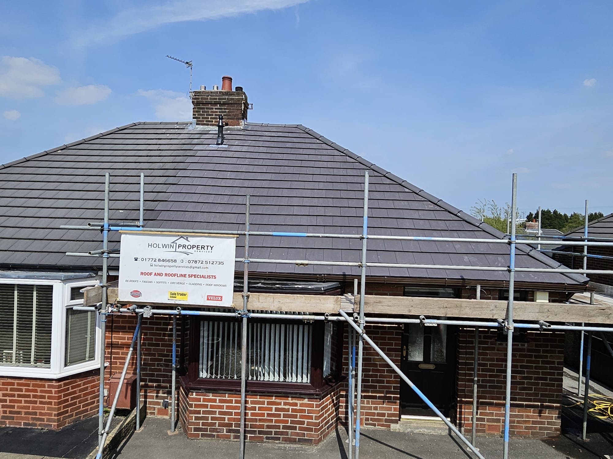 Dark tiled bungalow re-roof with scaffolding around a red-brick house