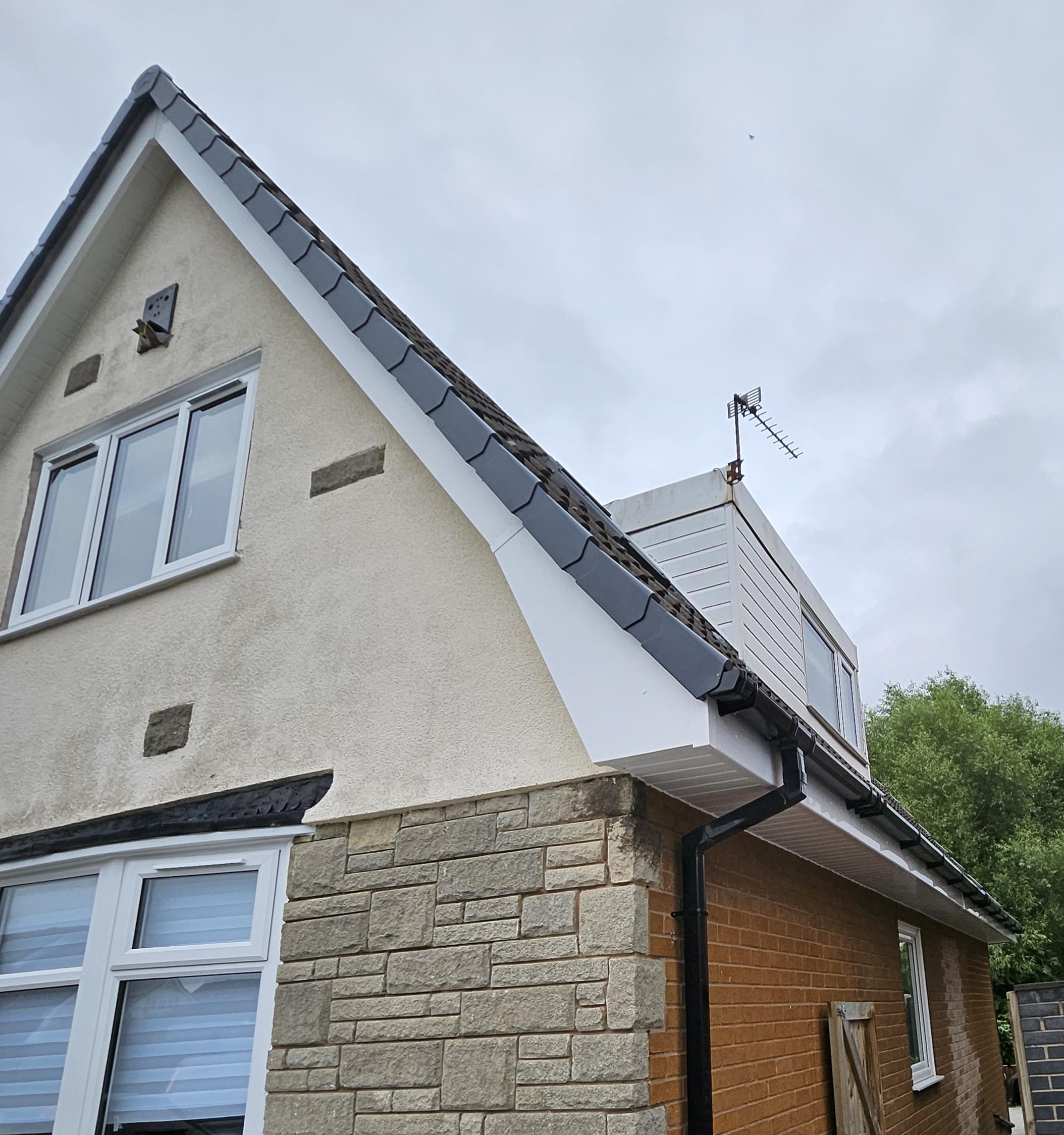 Dark tiles with white fascia, soffits and black guttering on a brick house