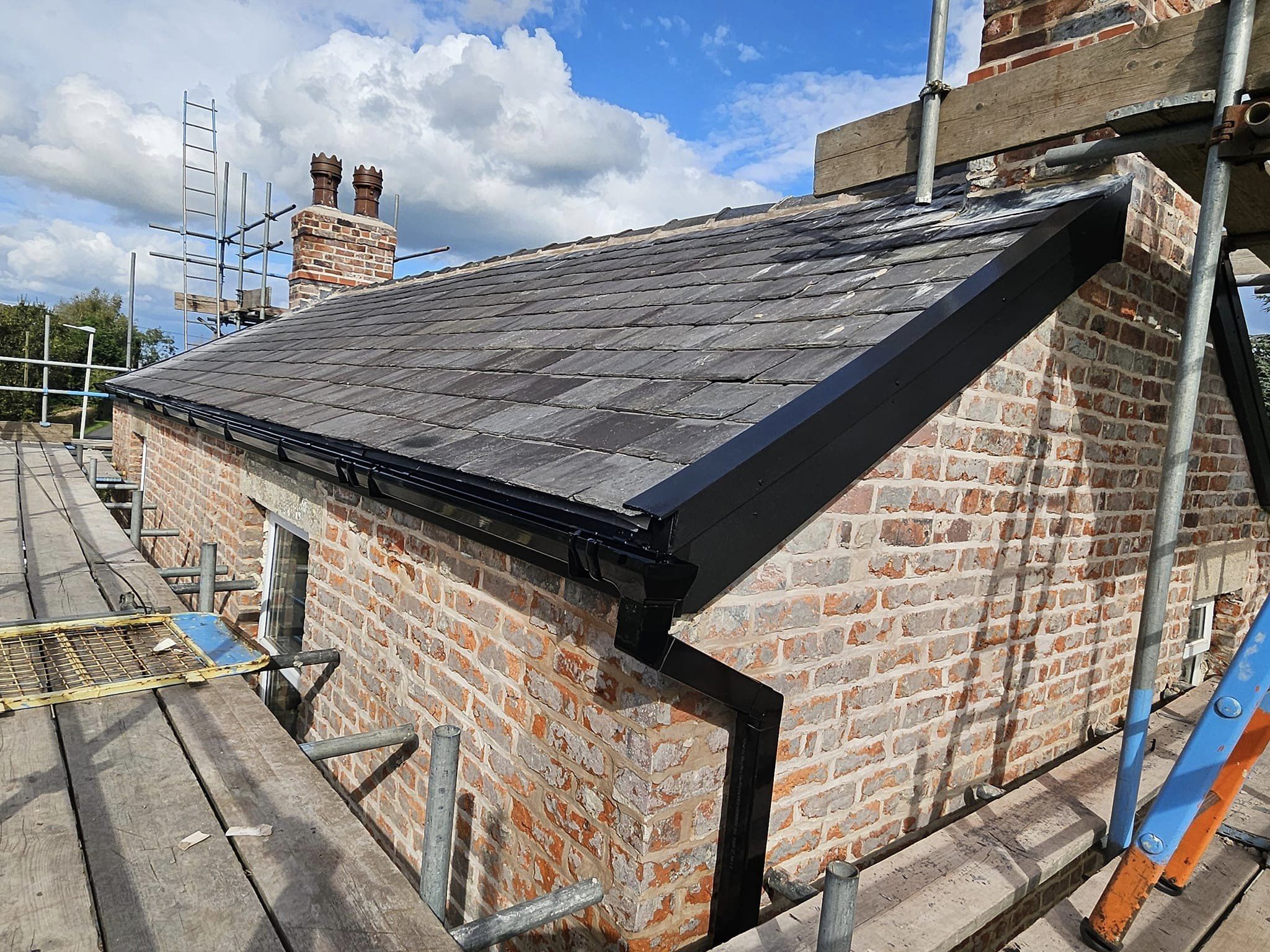 Dark tiled roof with new black fascia, gutter and downpipe on red brick