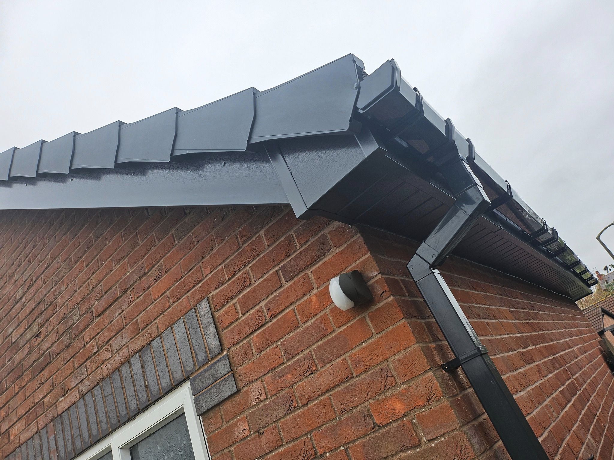 Black tiled verge, soffit and square downpipe on multi-toned brickwork